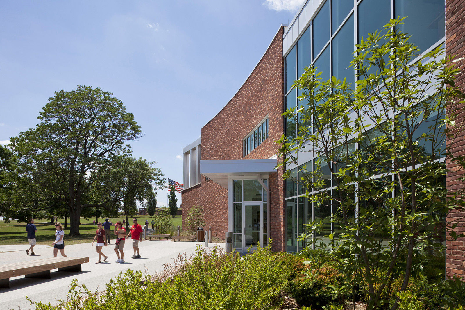 The incline of the brick wall gestures toward the flag, creating a visual dialogue between the fort and the visitor and education center.  The contrasting volumes of brick and zinc, and the gentle change of their heights in opposite directions, suggest a sense of motion and allude to the gentle waving of the flag above the fort. This movement is enhanced by the landscape design which incorporates berms, plantings, and vegetation that mimic the gentle curves in plan and vary in height.